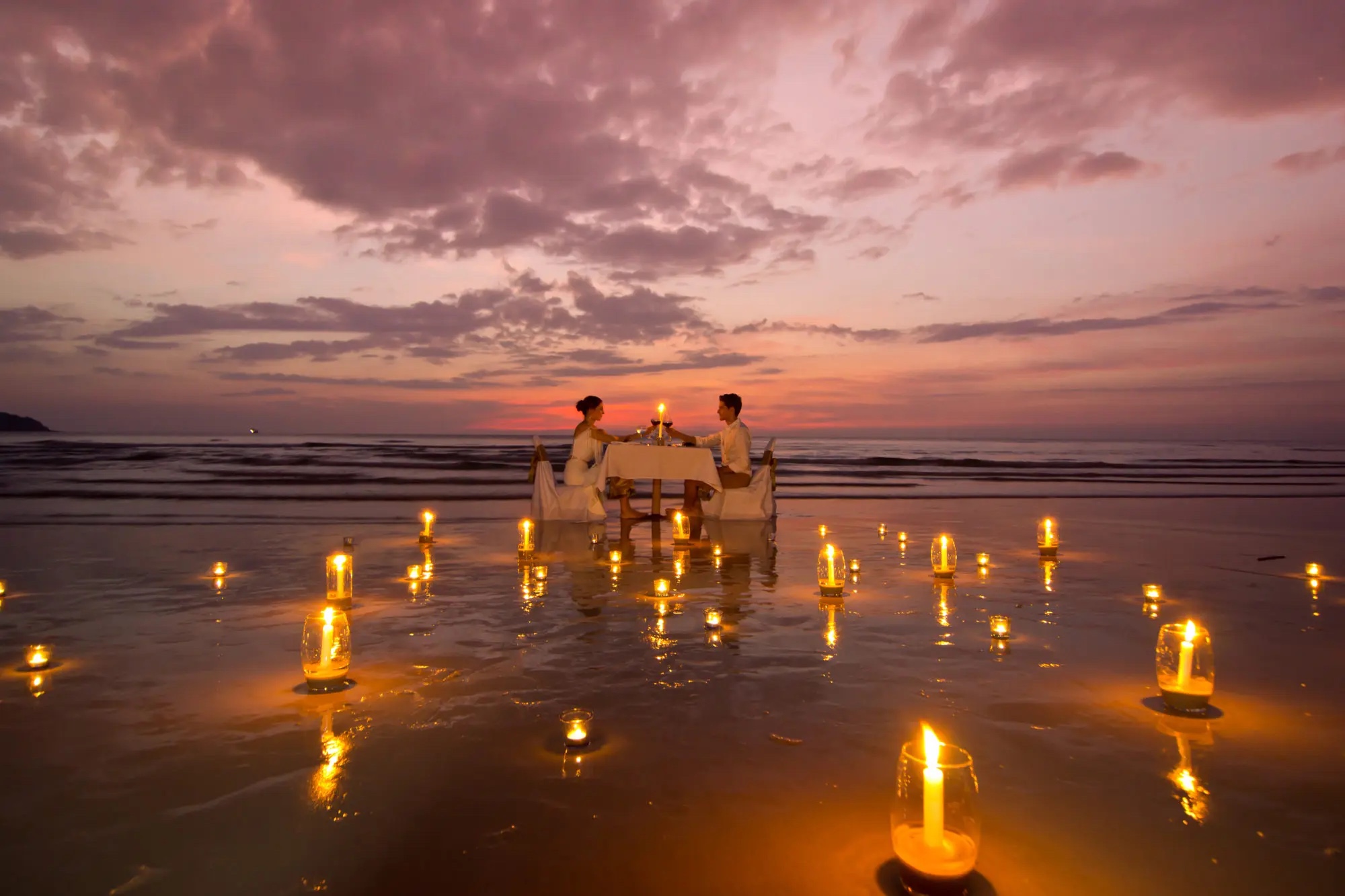 A couple walking along a bright southern beach beside stilt fishermen